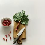 Fresh rhubarb stalk and leaves on a wooden cutting board with a knife, ready for cooking.
