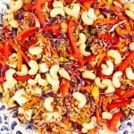 Vibrant quinoa salad with red peppers, carrots, cashews, and tofu on a decorative plate.