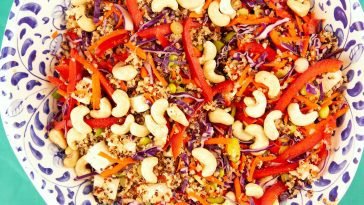 Vibrant quinoa salad with red peppers, carrots, cashews, and tofu on a decorative plate.