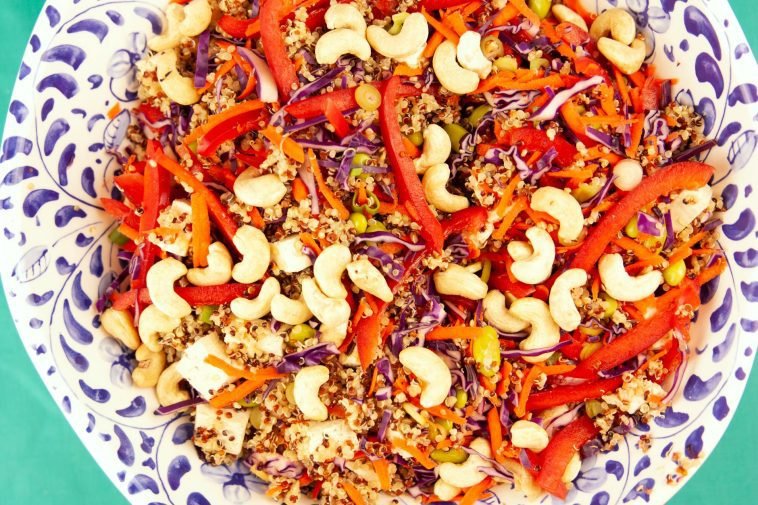 Vibrant quinoa salad with red peppers, carrots, cashews, and tofu on a decorative plate.