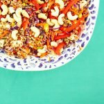 Vibrant quinoa salad with cashews, red peppers, and vegetables on a green background.