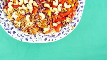 Vibrant quinoa salad with cashews, red peppers, and vegetables on a green background.